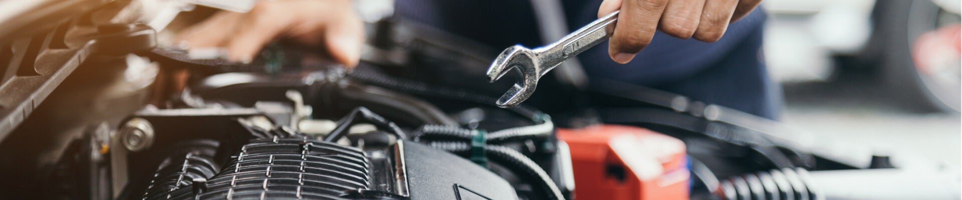 Close-up view of a mechanic holding a wrench over an open car engine bay.
